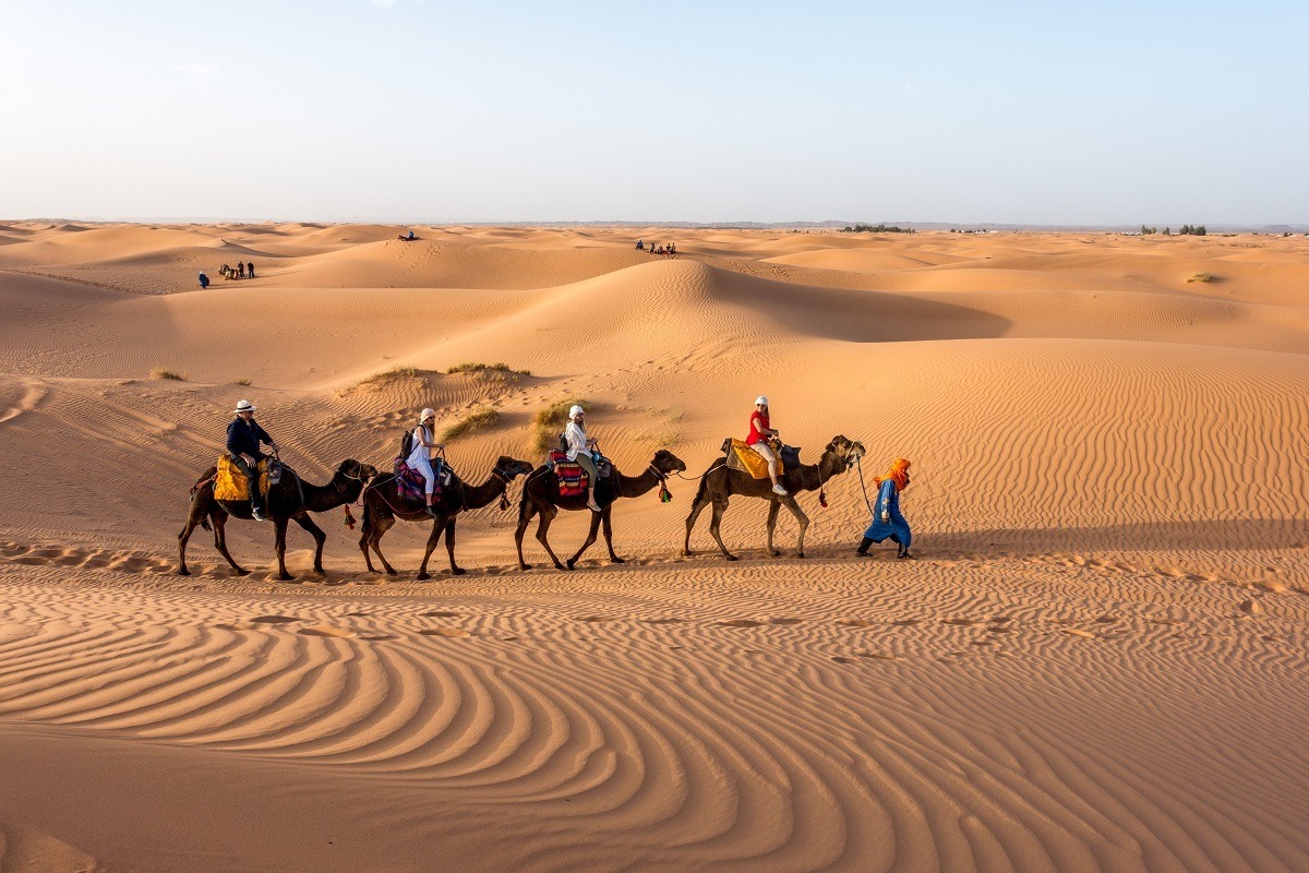 Line of people riding camels across sand dunes in Sahara desert