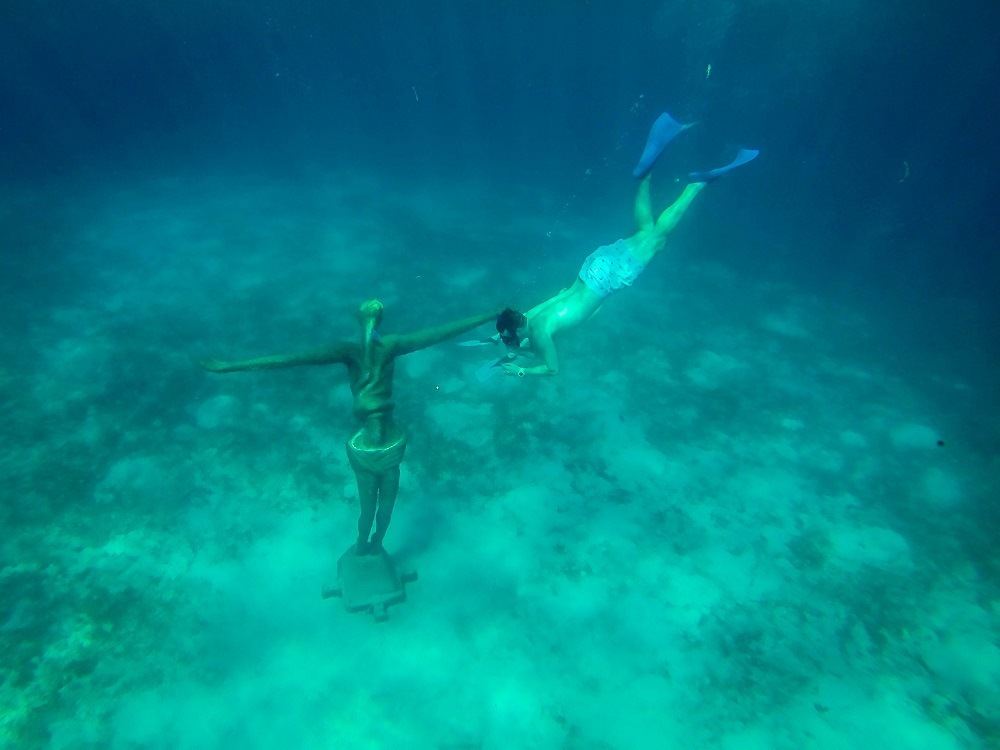Person snorkeling near an underwater statue